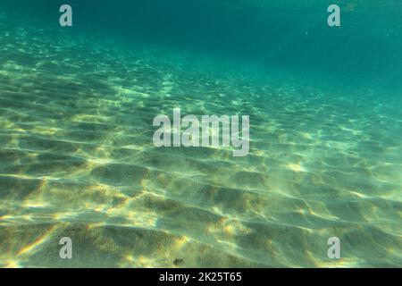 Sea bottom near sandy beach, sun lights on sand 'dunes'. Underwater photo, abstract marine background. Stock Photo