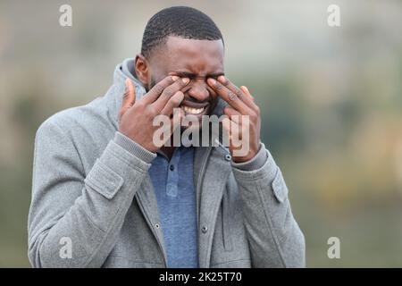 Man with black skin scratching eyes in winter Stock Photo