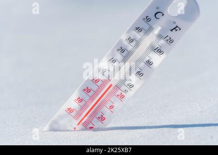 The thermometer lies on the snow and shows a negative temperature in cold weather on the blue sky.Meteorological conditions with low air and ambient temperatures.Climate change and global warming Stock Photo