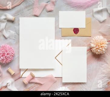 Wedding cards and envelopes between pastel flowers, silk ribbons and feathers on marble Stock Photo