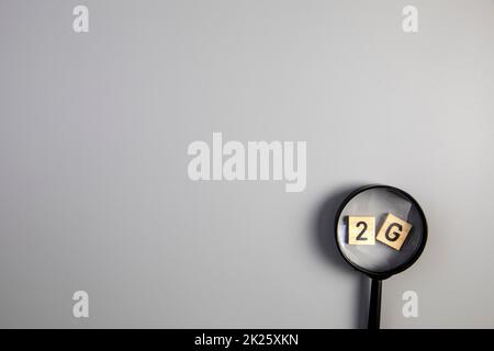 2G on gray background with magnifying glass for covi-19, ccoronavirus, pandemic rules concept top view copy space Stock Photo