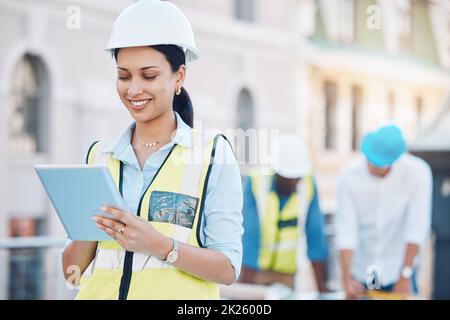 Construction, building and tablet with a woman architect working in the city on a build site with her team in the background. Engineer, designer and Stock Photo