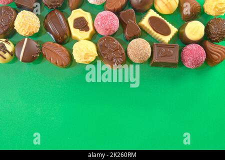 Chocolate pralines frame top view stock images. Chocolate candies on a green background. Chocolate frame top view. Chocolate pralines background with copy space for text. Border of different candies Stock Photo