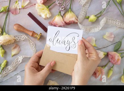 Hands with Card ALWAYS inside envelope near by pink flowers on a marble table Stock Photo