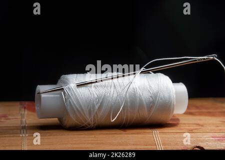 The thread is threaded through the eye of a sewing needle.Sewing and needlework classes.Workshop of hand craft and handmade.Workplace of the textile industry.The embroidery needle is stuck in a bobbin Stock Photo