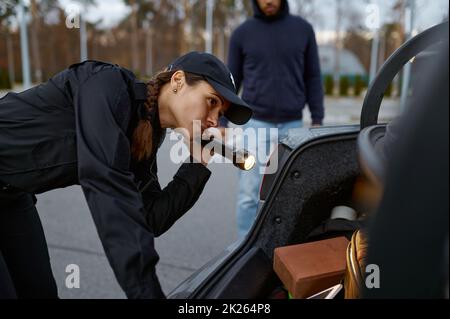 Woman police officer inspecting car with flashlight Stock Photo
