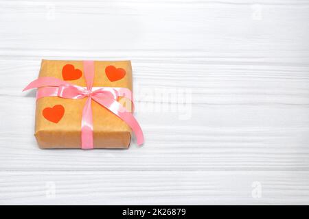 Eco gift boxes with pink ribbon and red felt hearts on white wooden background Stock Photo
