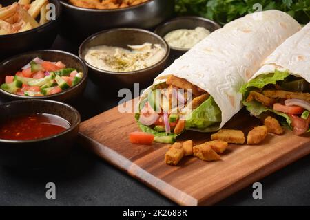 Shawarma Rolled Sandwich with Sauce and vegetables, Arab Traditional Food. Shawarma Doner kebab wrap with chicken, fries and pickles. Israeli Traditional homemade Shawarma on wooden cutting board. Stock Photo