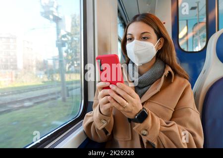 Young woman wearing face mask FFP2 KN95 against coronavirus reading on smartphone traveling on public transport. Healthcare, virus protection and travel safely concept. Stock Photo