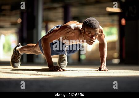 Side view of muscular black man in sportswear doing push ups during workout on street of modern downtown with urban background Stock Photo