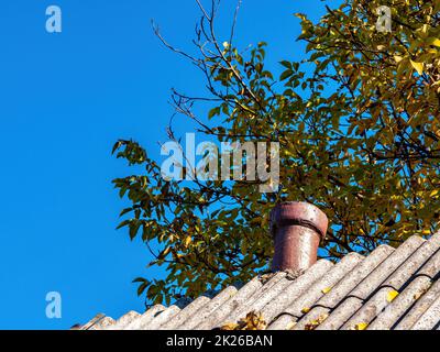 Chimney on the slate roof of the house against the blue sky. Stock Photo