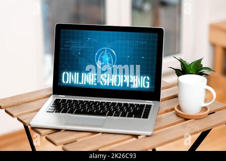 Conceptual caption Online Shopping. Conceptual photo ecommerce which let the consumer buy goods using the Internet Laptop Resting On A Table Beside Coffee Mug And Plant Showing Work Process. Stock Photo