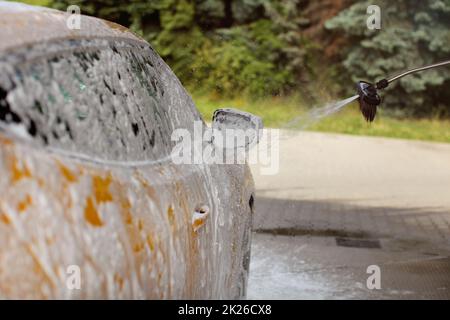 Side and side mirror of yellow car being washed in self service carwash, foam and shampoo spraying, drops in the air. Stock Photo