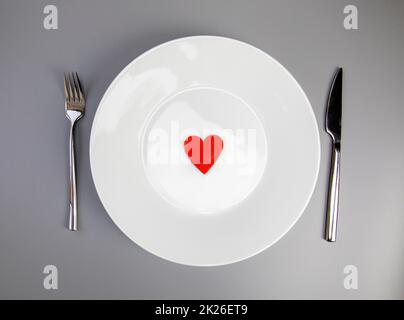 White plate with, fork and knife, red heart on grey background, flat lay. Valentine's day or medical health concept top view Stock Photo
