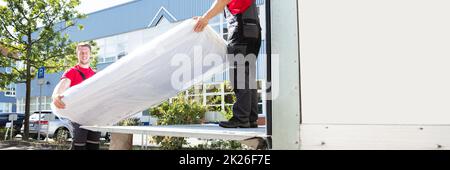 Young Men Unloading The Mattress From Truck On Street Stock Photo