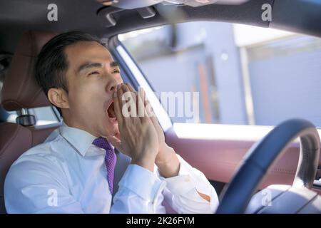 Young businessman looks tired yawning while driving the car Stock Photo
