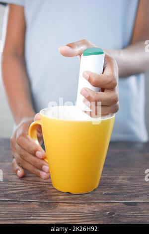 young man putting artificial sweetener in tea, Stock Photo