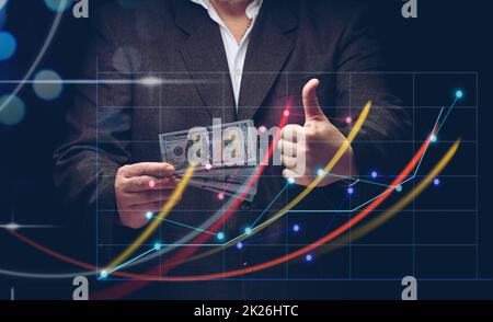 businessman in a suit holds a pack of paper american dollars against the background of a holographic chart with growing indicators. The concept of high business profitability, income growth Stock Photo