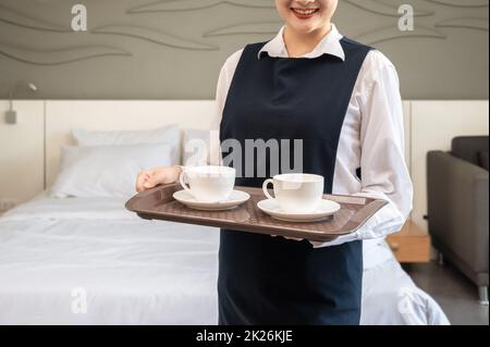 Smiling Chambermaid holding tray with cups of coffee.  Hotel room service concept. . Stock Photo