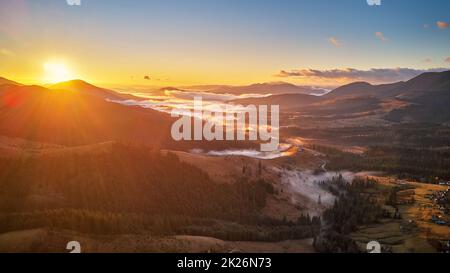 Colorful autumn sunrise over foggy woodland. Forest covered by low clouds. Fall rural landscape. Village in misty valley. Stock Photo
