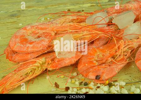 Frozen shrimps on a wooden white background with seasonings and crushed ice. Close-up of frozen prawns Stock Photo