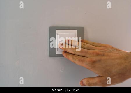 Close up view of a man pressing the light switch of the stay of a house Stock Photo