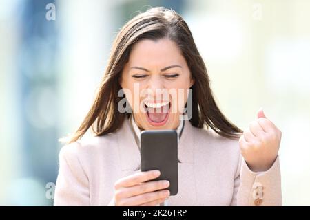 Excited businesswoman checking smart phone outdoors Stock Photo