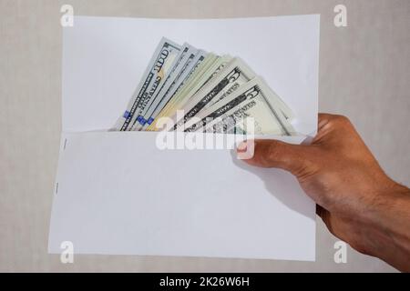Money in white envelope in the hands of a man. Dollars, a wad of dollars. Stock Photo
