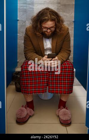 Businessman using his phone while sitting on toilet Stock Photo