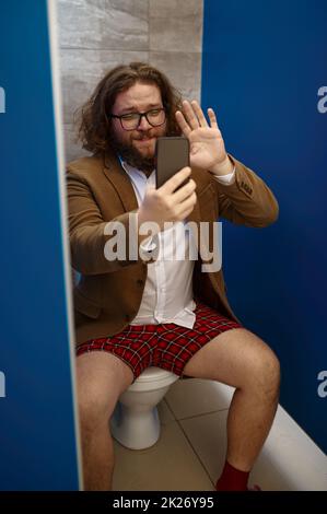 Businessman talking phone while sitting on toilet Stock Photo