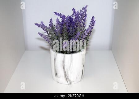 a violet and green artificial lavender plant with flowers and a marble vase on a white shelf Stock Photo