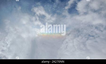 colorful rainbow was forming above white clouds after a rainstorm started and there was a gap between clouds to allow light to pass through making it Stock Photo