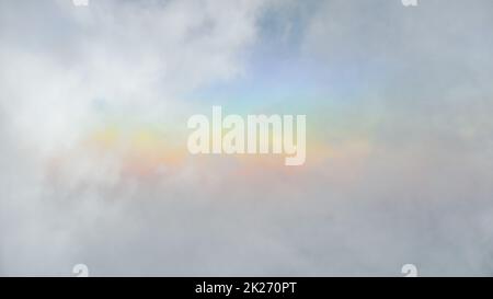colorful rainbow was forming above white clouds after a rainstorm started and there was a gap between clouds to allow light to pass through making it Stock Photo