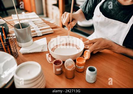 I use art to escape. Cropped shot of an unrecognizable woman sitting alone and painting a pottery bowl in her workshop. Stock Photo