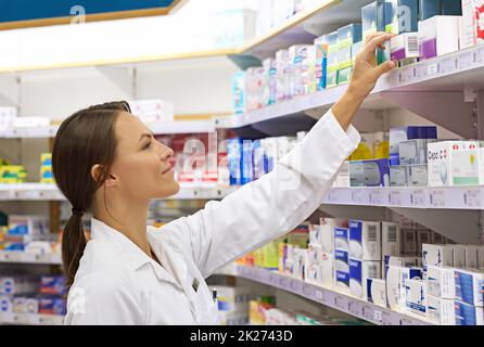 She knows her customer's needs. Shot of an attractive young pharmacist checking stock in an aisle. Stock Photo