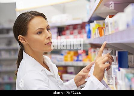 Tracking down prescriptions. Shot of an attractive young pharmacist checking stock in an aisle. Stock Photo