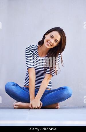 Free to be myself. Portrait of a beautiful young woman sitting with her legs crossed on the floor. Stock Photo