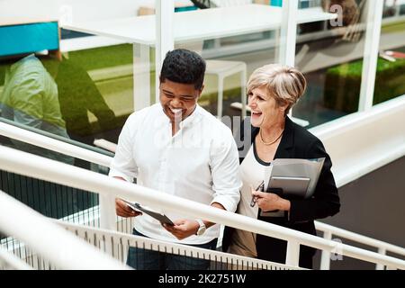 Levelling up together in business. Shot of two businesspeople walking up a staircase together in an office. Stock Photo