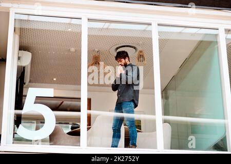 I hope this works out. Shot of a young businessman looking anxious while standing at a glass wall in an office. Stock Photo