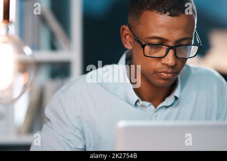 Hard work always pays off. Shot of a handsome young businessman working on his laptop during a late night shift at work. Stock Photo