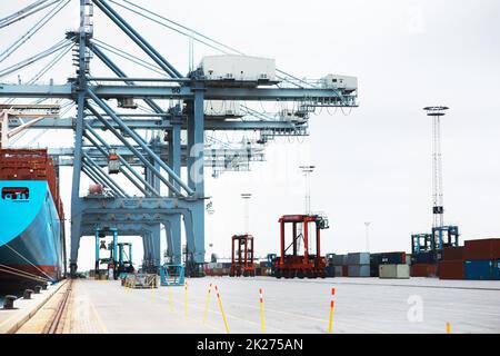 A normal day on the docks. A massive cargo ship moored at the harbor while being loaded with containers. Stock Photo