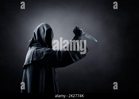 Hooded man with old knife in the dark Stock Photo
