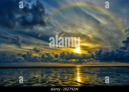 Rainbow over mud flat at low tide feahther clouds cumulus sunrise Stock Photo