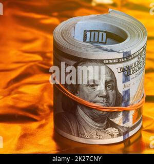 A roll of one hundred American dollars in close-up on a gold background. A big pile of cash dollars. One hundred dollar bills. Stock Photo