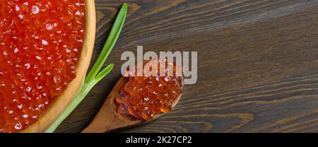 Red caviar in a wooden cup on a wooden background with a spoon. Stock Photo
