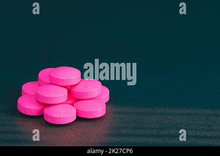 Pink pills are scattered on a black background. Stock Photo