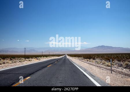 The Nevada Desert cut by a long infinite asphalt road under a clear blue sky