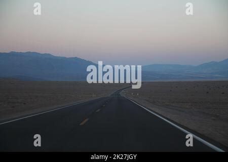 The never ending road during the dusk of a sunset in the Death Valley desert Stock Photo