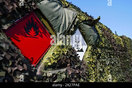 Flammable and dangerous - Hazardous marine pollutant substance - sign on brown green metal side of army petrol or fuelling vehicle covered with camouflage net Stock Photo