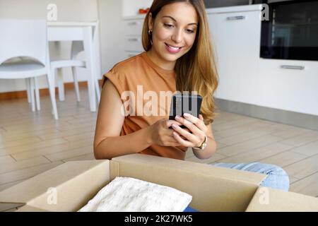 Online store selling clothes on website working on smartphone ecommerce business from home. Woman packing clothing purchase in shipping packages for delivery. Stock Photo